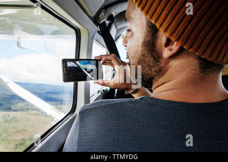 Vue arrière de l'homme photographie paysage par smart phone à partir de la fenêtre de l'avion Banque D'Images