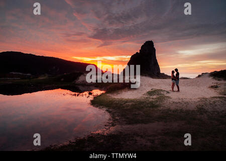 Couple romantique sur le sable contre le ciel au coucher du soleil Banque D'Images