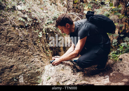 Sac à dos avec Male hiker photographing par caméra pendant accroupi sur rock formation Banque D'Images