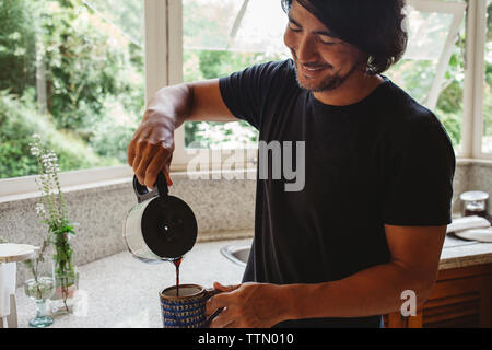 Smiling man pouring coffee en étant debout dans la cuisine Banque D'Images