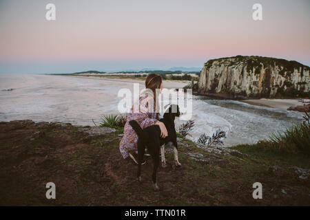 Vue de côté de femme accroupie par chien sur la plage pendant le coucher du soleil à hill Banque D'Images