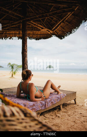 Woman in bikini relaxing on bed at beach Banque D'Images