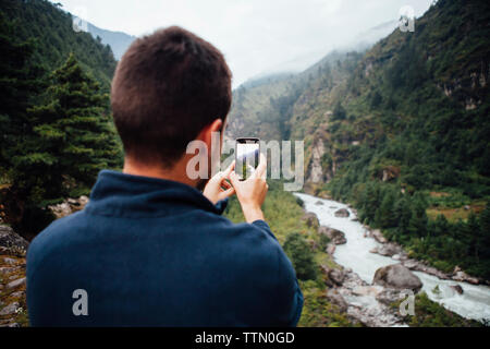 Vue arrière du male hiker photographing river au milieu de montagnes à Parc national de Sagarmatha Banque D'Images