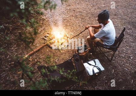 Portrait de randonneur assis sur chaise de camping par feu de forêt Banque D'Images