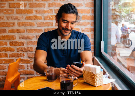 Mature man using smart phone against brick wall in cafe Banque D'Images