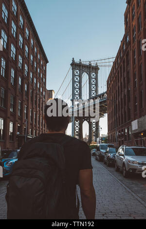Vue arrière de l'homme avec sac à dos à la recherche de pont de Manhattan en étant debout on city street Banque D'Images