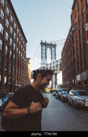 Vue latérale du sac à dos avec l'homme debout contre Manhattan Bridge on city street Banque D'Images