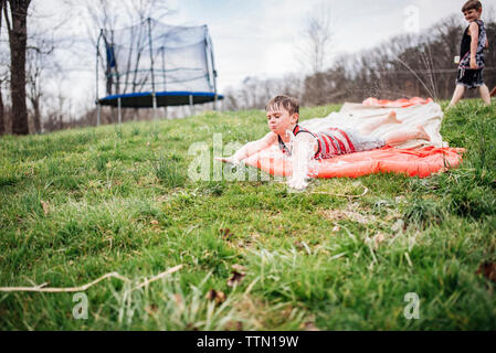 Garçon glisser sur un toboggan lorsque frère marcher en arrière-plan du park Banque D'Images