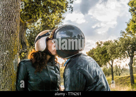 Couple romantique tout en se tenant par des arbres contre le ciel au coucher du soleil Banque D'Images