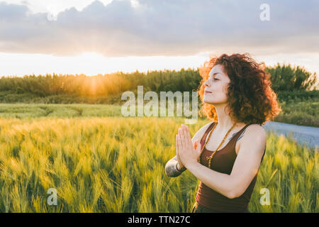 Femme méditant en position debout au niveau de l'exploitation contre ciel nuageux pendant le coucher du soleil Banque D'Images