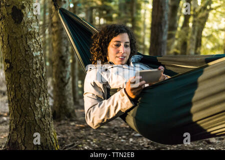 Femme à l'aide de smart phone en position allongée sur un hamac en forêt