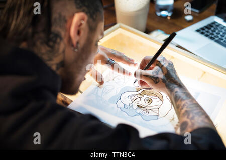 Jeune artiste de tatouage dessin sur table en studio Banque D'Images