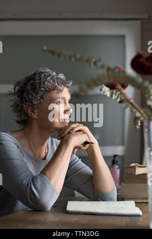 Thoughtful mature woman sitting by table à la maison Banque D'Images
