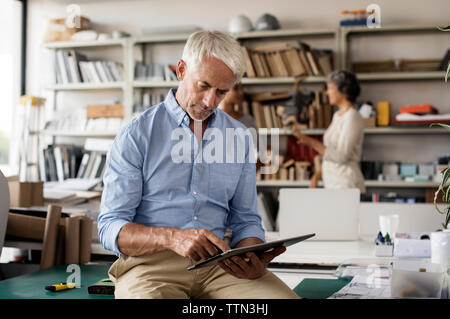 Homme d'intérieur à l'aide de l'ordinateur tablette alors que collègues femmes discutant en arrière-plan Banque D'Images