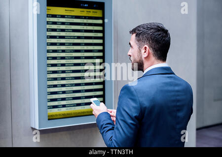 Vue arrière du businessman holding smart phone pendant la lecture arrivée départ à subway station Banque D'Images