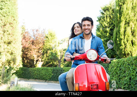 Smiling couple riding on motor scooter à park Banque D'Images