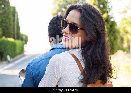 Vue arrière portrait of smiling woman riding avec man on motor scooter Banque D'Images