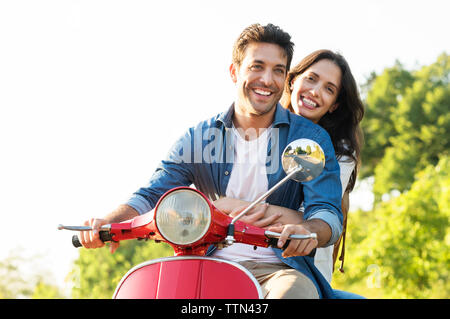 Heureux couple riding sur scooter contre ciel clair Banque D'Images