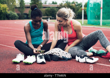 Les amis de l'athlète looking at mobile phone while sitting on track Banque D'Images