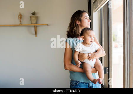 Mother with baby boy standing by window at home Banque D'Images