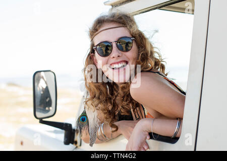 Happy woman wearing sunglasses peeking through car window Banque D'Images