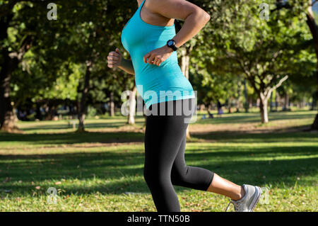 Portrait woman jogging on grassy field contre des arbres en parc Banque D'Images