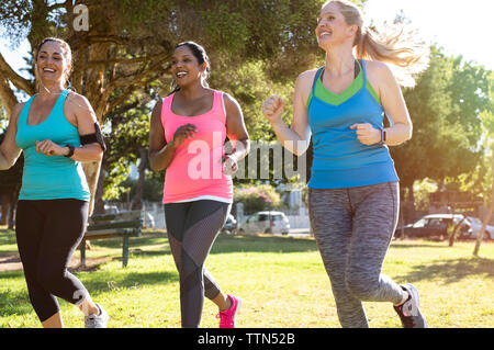 Low angle view of happy friends jogging on grassy field in park Banque D'Images