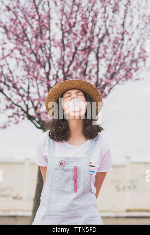 Young woman blowing bubble gum debout contre Cherry Tree at park Banque D'Images