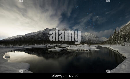 Vue du lac tranquille à l'encontre de montagnes aux sommets enneigés au parc d'état de Chugach, pendant la nuit Banque D'Images