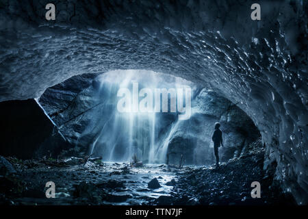 Side view of man looking at waterfall tout en se tenant dans la caverne de glace Banque D'Images