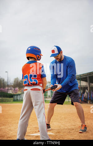 Aider l'entraîneur garçon en jouant au baseball sur terrain Banque D'Images