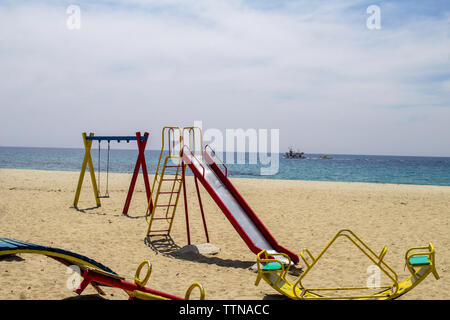 Aire de jeux située sur la plage de Nea Skioni, Halkidiki, Grèce avec un chalutier de pêche dans l'arrière-plan. Banque D'Images