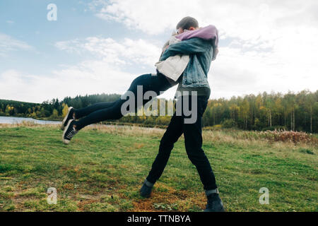 Low angle view of young couple embracing while standing on grassy field against cloudy sky in forest Banque D'Images