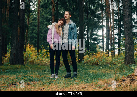 Jeune couple standing on grassy field contre des arbres en forêt Banque D'Images