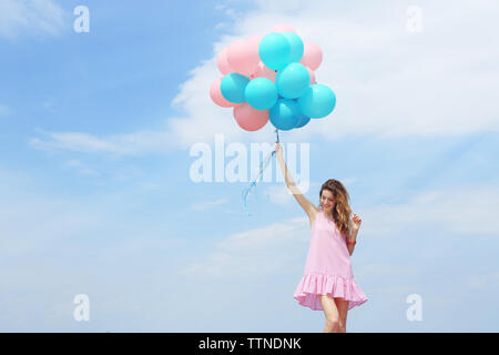 Belle jeune femme avec des ballons colorés sur fond de ciel bleu Banque D'Images