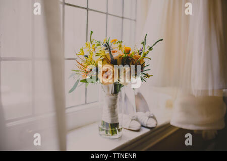 Vase à fleurs et des chaussures sur appui de fenêtre par robe de mariage Banque D'Images