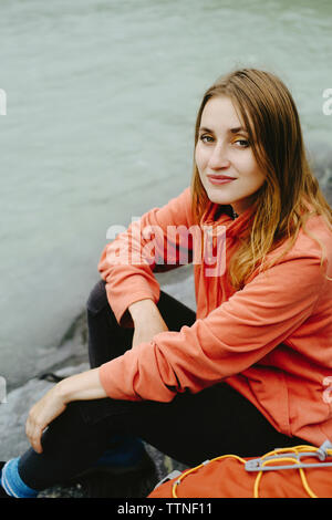 High angle portrait of female hiker with backpack assis à riverbank Banque D'Images