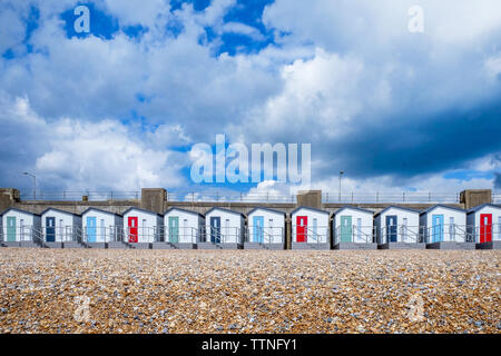 Une ligne de 12 nouvelles cabines de plage qui traverse le centre de l'image de rouge, bleu et vert, portes et balcons, ci-dessous est une plage de galets et un jaune Banque D'Images