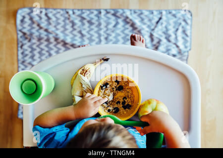 Vue de dessus de garçon de manger des aliments dans une chaise haute Banque D'Images