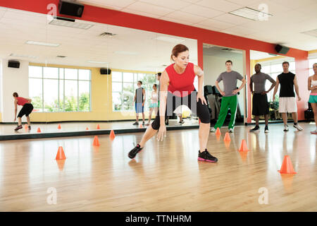Les clients à la recherche à l'instructeur de conditionnement physique l'exercice entre les cônes à gym Banque D'Images