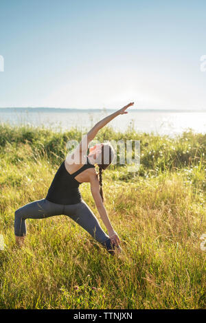 L'angle de côté Woman practicing yoga pose sur les champs par mer au cours de journée ensoleillée Banque D'Images