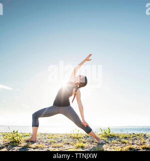 L'angle de côté Woman practicing yoga pose à plage en journée ensoleillée Banque D'Images