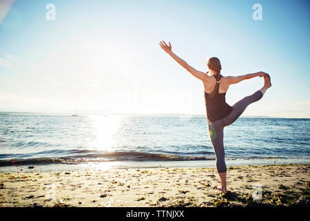 Vue arrière de la main pour woman practicing yoga pose au gros orteil plage en journée ensoleillée Banque D'Images