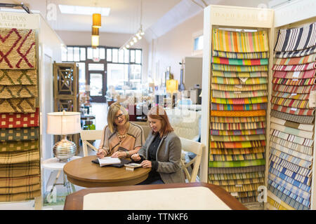 Les femmes propriétaires de discuter tout en étant assis à table in furniture store Banque D'Images