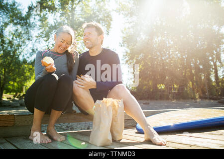 Couple eating food while sitting on pier contre ciel lors de journée ensoleillée Banque D'Images