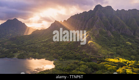 Vue idyllique de la montagne par le lac contre ciel nuageux pendant le coucher du soleil Banque D'Images