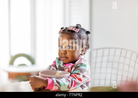 Thoughtful girl holding bol petit déjeuner à table dans la cuisine Banque D'Images