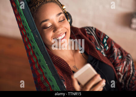 Happy woman listening music par smart phone sur le hamac à la maison Banque D'Images