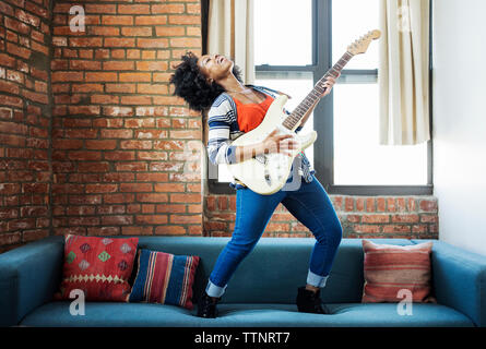 Femme heureuse de chanter tout en jouant de la guitare sur canapé Banque D'Images