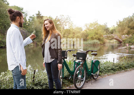 Heureux homme donnant à fleur pour petite amie tout en se tenant par le lac Banque D'Images